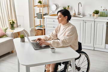 A disabled woman in a wheelchair works remotely on her laptop in the kitchen, showcasing digital...