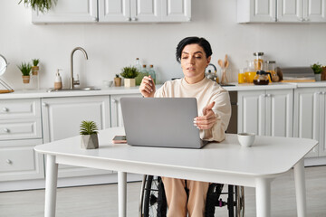 A disabled woman in a wheelchair is focused on her laptop at a kitchen table, engaging in remote work or leisure activities.