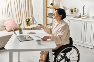 A disabled woman in a wheelchair working on a laptop in her kitchen, showing empowerment and...