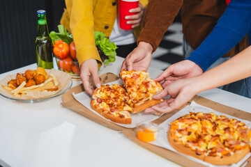 .Young Asian students gather with friends for a pizza party, laughing and sharing slices. Enjoying fast food delivery, they embody diversity and togetherness in a relaxed, enjoyable lifestyle.