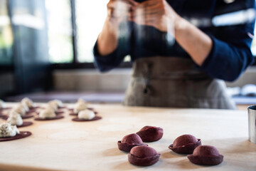 The essence of Italian gastronomy. A chef's deft woman hands create a beetroot pasta masterpiece, the art of culinary finesse. Main focus on Handcrafted tortello.