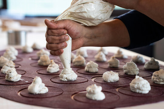 Artisanal mastery in Italian tortello making, beetroot pasta meets ricotta. The chef's hands skillfully pipe the heart of gourmet tradition.