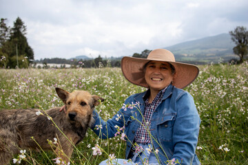 Smiling adult woman in a rural setting in the Andes mountains. The woman is wearing a sun hat in a green meadow
