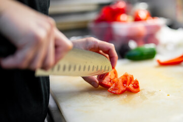 Chef skillfully slicing fresh red tomatoes on a cutting board in a kitchen, highlighting culinary technique and freshness