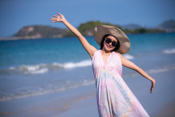 Happy sexy Asian traveller woman wear colorful beach dress and hat show enjoys on tropical beach vacation in summer holidays	