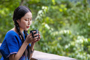 Portrait  of a beautiful asian woman wearing traditional  dresses pose holding and drinking hot coffee by sitting on balcony looking mountains and green nature is outdoor relaxed concept. - 796759806
