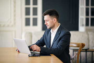 A focused executive in a sleek suit works intently on a laptop at an elegant wooden desk in a...