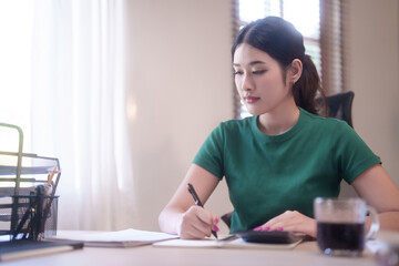 Young asian student women doing homework and using calculator with finance to taking notes in notebook after studying lecture webinar in online class and learning knowledge remote education from home