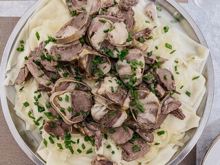 The Kazakh national dish is beshbarmak. thinly sliced beef and lamb on a large round plate with...