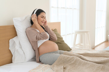 Happy pregnant woman with headphones listening to mozart music and lying on bed, pregnancy concept