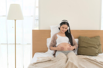 Happy pregnant woman with headphones listening to mozart music and lying on bed, pregnancy concept