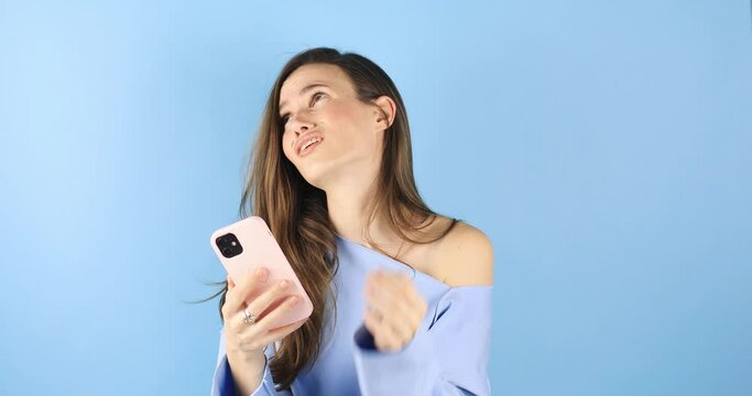Close up young girl sad while read a message about broke up. Sad young woman isolated on blue background looking at smartphone screen and be melancholy after receiving bad news. Bad mood.