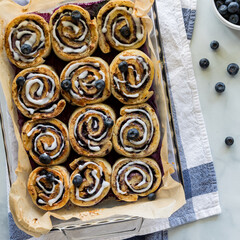 Fototapeta premium A dozen freshly baked blueberry cinnamon rolls, glazed with vanilla icing.