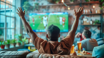 Young people spend the evening watching a football match. They are comfortably ensconced on the couch, completely immersed in the atmosphere of the game and raise their hands high in the air