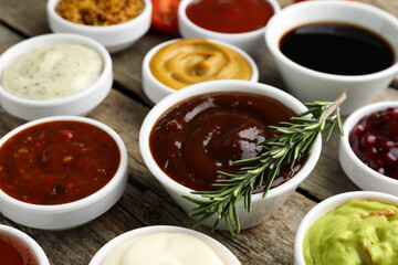 Different tasty sauces in bowls and rosemary on wooden table, closeup