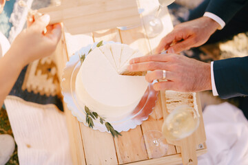 Bride holds out a wooden plank to groom, who cuts a piece of the wedding cake. Cropped. Faceless