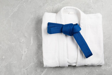Blue karate belt and white kimono on gray marble background, top view. Space for text
