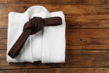 Brown karate belt and white kimono on wooden background, top view. Space for text