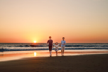 Three kids silhouettes running and jumping on beach at sunset. happy family, two school boys and one little preschool girl. Siblings having fun together. Bonding and family vacation.