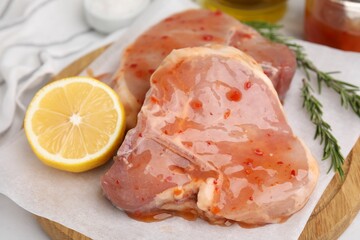 Board with raw marinated meat, lemon and rosemary on white table, closeup