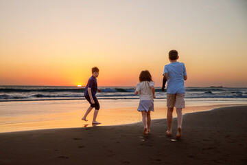 Three kids silhouettes running and jumping on beach at sunset. happy family, two school boys and one little preschool girl. Siblings having fun together. Bonding and family vacation.