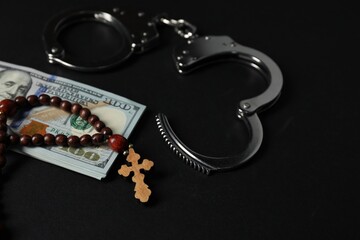 Dollars, handcuffs and prayer beads on black table