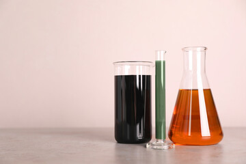 Test tube, beaker and flask with different types of oil on grey table against light background, space for text