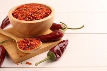 Chili pepper flakes and pods on white wooden table, closeup. Space for text