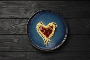 Heart made with spaghetti and sauce on black wooden table, top view.