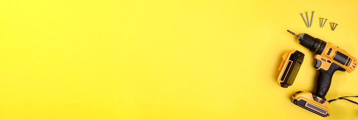 Banner: cordless electric yellow screwdriver, battery and screws on a yellow background. Copy space. Concept of construction, repair, electrical equipment.