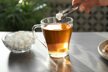 Woman adding sugar cube into cup of tea at dark table, closeup