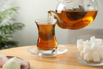 Pouring tasty tea into cup at wooden table indoors