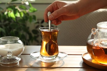 Woman stirring sugar in tea at wooden table indoors, closeup
