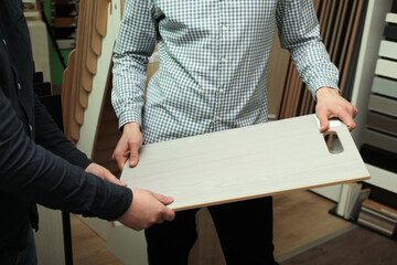 Men holding sample of wooden flooring in shop, closeup