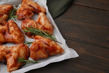 Raw marinated chicken wings and rosemary on wooden table, closeup. Space for text