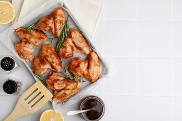 Raw chicken wings, rosemary, marinade and spices on light tiled table, flat lay. Space for text