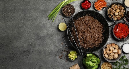 Wok with noodles, chicken and other products on grey table, flat lay. Space for text