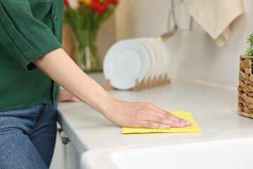 Woman cleaning table with sponge wipe in kitchen, closeup