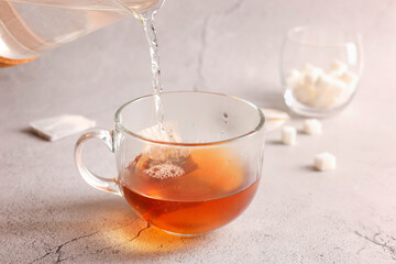 Pouring hot water into cup with tea bag on light grey textured table, closeup