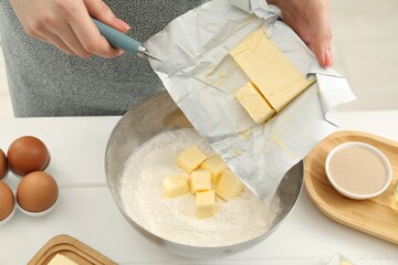 Woman adding fresh butter into bowl with flour at white wooden table, closeup