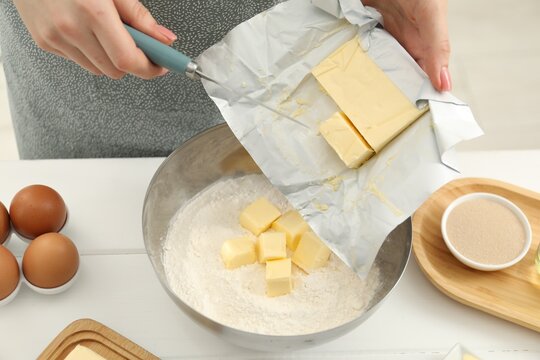 Woman adding fresh butter into bowl with flour at white wooden table, closeup