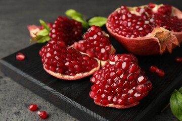 Cut fresh pomegranate and green leaves on grey table, closeup