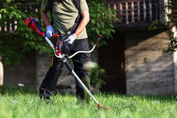 Man mowing grass with a string trimmer - 796792208