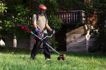 Man mowing lawn with cordless string trimmer