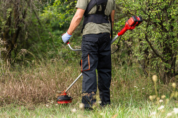 Man trimming grass with a cordless string trimmer