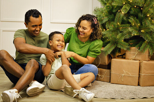 Familia Parda com tra&ccedil;os brasileiros com homem, mulher e um menino crian&ccedil;a, em uma sala com uma decora&ccedil;&atilde;o de natal na cor verde.