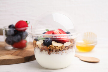 Tasty granola with berries, yogurt and almond flakes in plastic cup on white table, closeup