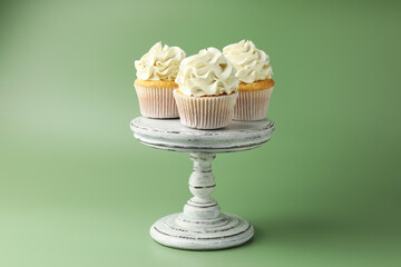 Tasty vanilla cupcakes with cream on green background