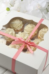 Tasty cupcakes with vanilla cream in box and orchid flowers on white wooden table, closeup