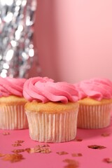 Delicious cupcakes with bright cream and confetti on pink background